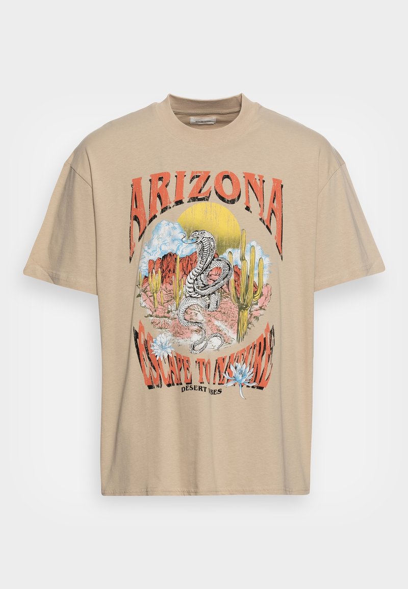 T-shirt oversize beige présentant un graphique coloré d'un serpent, des cactus et le texte "ARIZONA ESCAPE TO NATURE". Matière en coton doux.