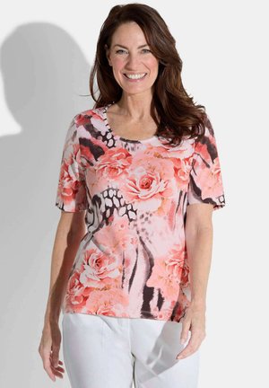Top à manches courtes en tissu doux, présentant un motif floral rose avec des accents noirs et un col rond. Un pantalon blanc uni complète l'ensemble.