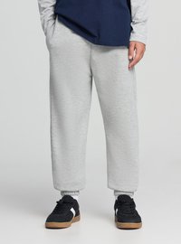 Pantaloni della tuta grigi in tessuto morbido, con polsini elasticizzati e vestibilità comoda. Abbinati a scarpe da ginnastica nere con dettagli bianchi.