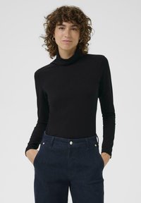 Svart polokrage i en figurnära design, tillverkad av ett slitstarkt tyg. Matchas med högmidjade mörkblå jeans som har framfickor och metalldetaljer.