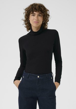 Haut à col roulé noir au design ajusté, fabriqué en tissu lisse. Associé à un jean bleu foncé taille haute avec des poches avant et des accents métalliques.