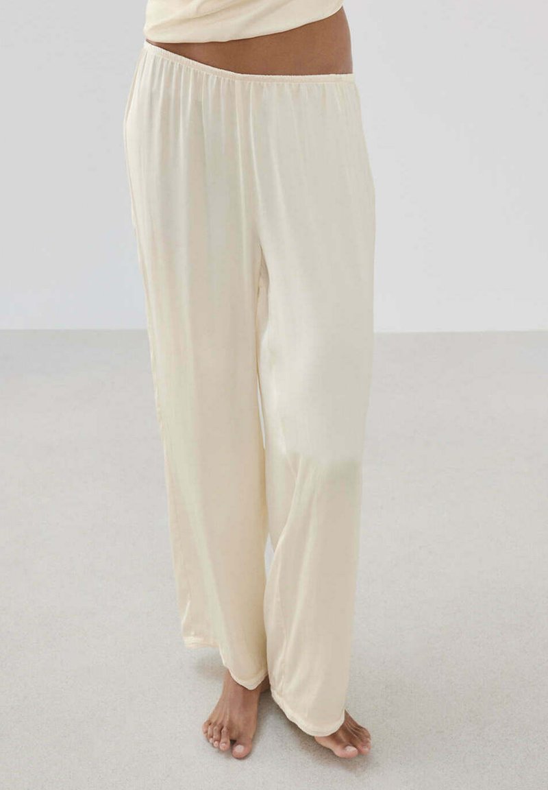 Pantalon ample de couleur crème porté pieds nus, avec une taille élastique, montré de la taille jusqu'aux pieds sur un fond clair.