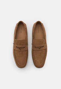 Brown suede slip-on shoes with a smooth texture, featuring a stitched accent and a curved cutout on the front panel.