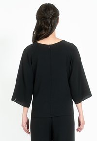 Top nero con scollatura rotonda, maniche a tre quarti a campana e chiusura con zip sul retro. Realizzato in tessuto morbido, presenta cuciture minime.