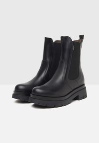 Botas de tobillo negras con piel suave, paneles elásticos a los lados y una suela de goma gruesa con un ligero tacón. Incluye una lengüeta lateral.