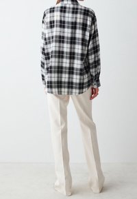 Chemise à carreaux noir et blanc en tissu doux, avec des manches longues, des poignets boutonnés et une coupe décontractée, associée à un pantalon couleur crème.