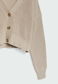 Beige stickad cardigan med V-ringning, knappstängning och ribbade nertill, med en strukturerad stickning och kort design.