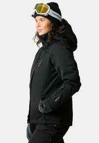 Black ski jacket with a hood, featuring zippered pockets and cuffs. Paired with a black beanie and ski goggles with a yellow tint.