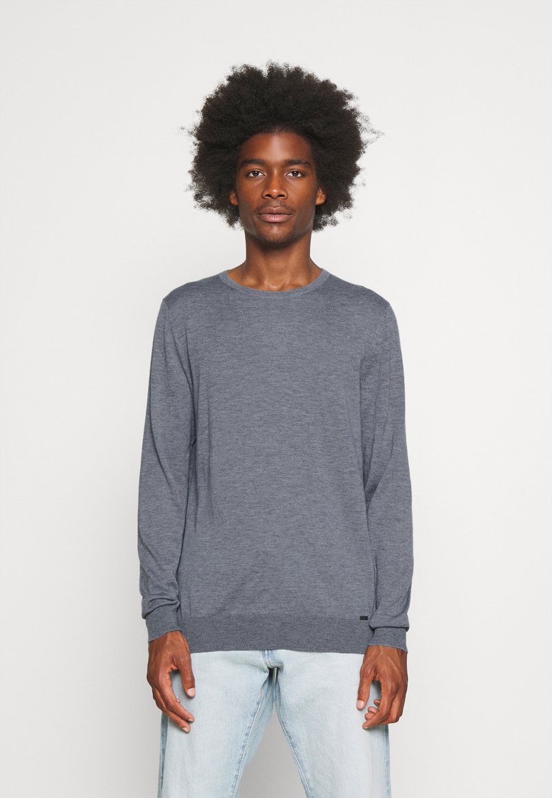 Long-sleeve crewneck sweater in heathered dark gray fabric. Features ribbed cuffs and hem, with a subtle logo tag at the bottom left.