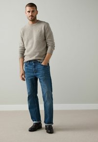 Lys grå, tekstureret striktrøje med op卷ede ærmer, parret med blå lige bukser. Sorte lædersko med en subtil mønsterdetalje.