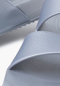 Light blue slides with textured synthetic material, two wide straps, and a durable sole featuring a patterned grip.