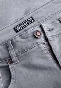 Šedé džíny z denimu s knoflíkovým a zipovým zapínáním, se značkovou etikettou. Hladká textura, zesílené švy a měděné detaily.