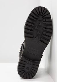 Suola di stivale nera con motivi di battistrada profondi, taglia contrassegnata come 37, appoggiata su una superficie bianca.