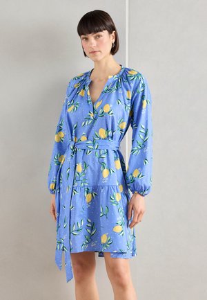 Blue dress featuring a lemon and leaf print, gathered neckline, long sleeves, a tie belt, and a tiered hem. Soft fabric with a light texture.