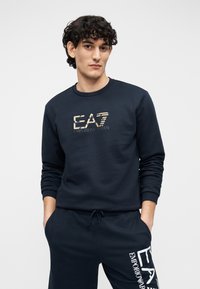 Sügavsinine pusa pehmest materjalist, millel on kuldne EA7 logo rinnal. Pika käistega, mansettidega varrukad. Sobivad püksid komplektis.