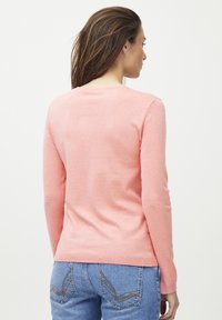 Pull rose à manches longues avec un col rond, texture douce et design cintré, associé à un jean en denim bleu avec des coutures décoratives.