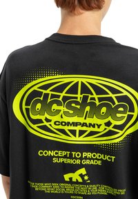 Czarna bawełniana koszulka z dużym żółtym wzorem graficznym przedstawiającym glob, nazwę marki i tekst, a także wzory w kropki oraz luźny krój.