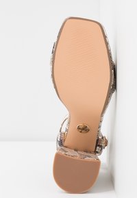 Sandale à talon avec un motif texturé de peau de serpent multicolore. Elle présente une semelle en caoutchouc marron clair et un accent rond avec un logo doré.