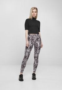 Leggingse sa zebrastripednim uzorkom u crno-bijeloj boji, izrađene od rastezljivog materijala, uparene s crnim kratkim topom i crnim sjajnim cipelama.