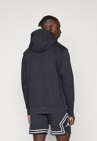 Felpa nera con un grande cappuccio, realizzata in materiale morbido. Indossata con pantaloni corti scuri con strisce bianche e un logo di lato.