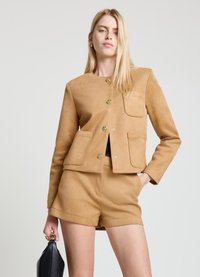 Tan suede jacket featuring a round neckline, front patch pockets, golden buttons, and a cropped design, paired with matching shorts.