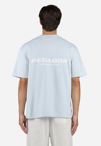 Svijetloplavi pamučni majica kratkih rukava, s bijelim tekstom "PEGADOR" i "CERTIFIED AUTHENTIC STREETWEAR" na leđima.