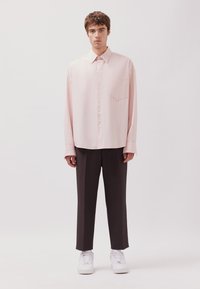 Helles pink gestreiftes Hemd mit klassischem Kragen und einer Brusttasche, kombiniert mit dunklen Hosen und weißen Turnschuhen. Sanfte Stofftextur.
