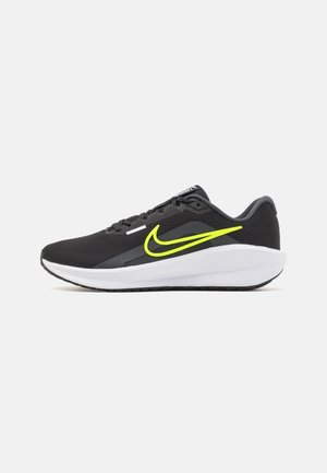 Zapatillas deportivas negras con parte superior de malla, que presentan un prominente swoosh amarillo, media suela blanca y suela exterior negra texturizada.