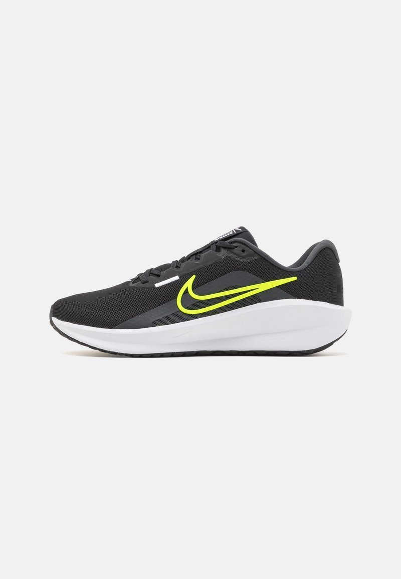 Sorte atletiske sko med en mesh-overdel, der har en iøjnefaldende gul swoosh, hvid mellemsål og struktureret sort ydersål.