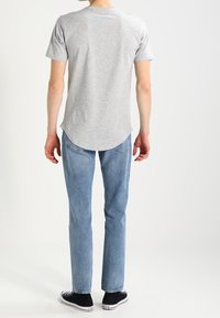 Camiseta gris de manga corta con dobladillo curvado, combinada con jeans azul claro y zapatillas negras con suelas blancas.