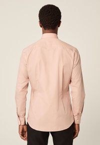 Hellrosa langärmeliges Hemd mit klassischem Kragen, glattem Stoff, geradem Saum und geknöpften Manschetten. Rückansicht zeigt eine taillierte Passform.