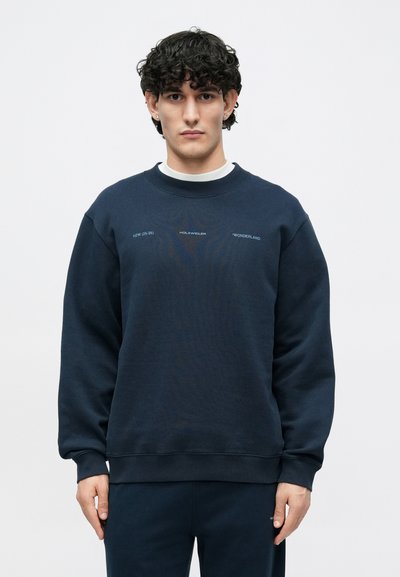 Temno modra bombažna mešana majica z okroglim izrezom, rebrastimi manšetami in potiskanim napisom spredaj. Mehka tekstura z sproščenim krojem.