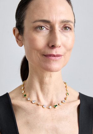 Gold necklace featuring an alternating pattern of clear and green gemstones, with varied shapes including round, square, and rectangular.