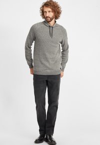 Suéter de punto gris con capucha, con un patrón texturizado y un cordón ajustable. Combinado con pantalones negros y zapatos negros.
