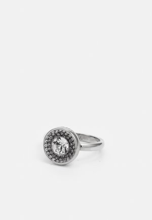 Bague en argent avec une grande pierre précieuse claire au centre entourée de petites pierres claires dans un sertissage circulaire sur un fond blanc uni.