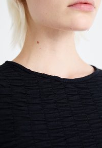 Svart teksturert stoff med en rynket design. Nærbilde av en rund halslinning, som viser fine detaljer og søm.
