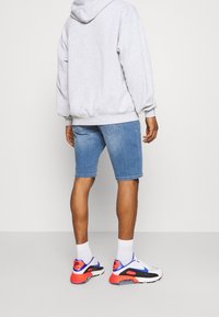 Sudadera con capucha gris, shorts de mezclilla azul claros y zapatillas coloridas con suelas blancas. Vista trasera, mostrando un corte relajado y un estilo casual.