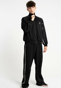 Czarny sportowy dres z zamkiem błyskawicznym i dopasowanymi spodniami, z białymi paseczkami po bokach. Gładka tekstura i luźny krój.