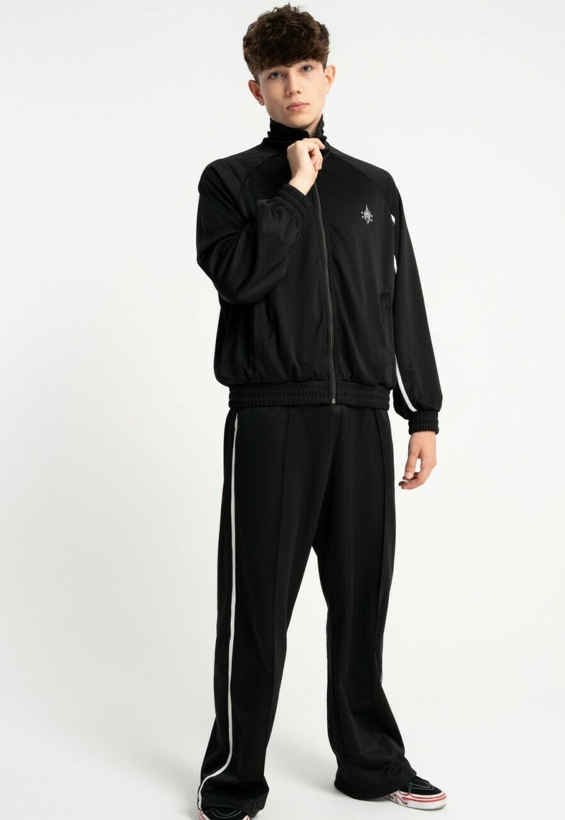 Czarny sportowy dres z zamkiem błyskawicznym i dopasowanymi spodniami, z białymi paseczkami po bokach. Gładka tekstura i luźny krój.