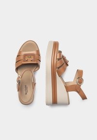 Sandali con zeppa in pelle marrone, dotati di ampie cinghie incrociate, una cinghia regolabile alla caviglia e una suola in gomma beige con una leggera texture.