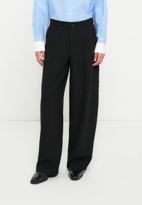 Μαύρο παντελόνι με φαρδύ πόδι και ομαλή υφή, με κούμπωμα με κουμπί και πιέτες μπροστά. Συνδυάζεται με ανοιχτό μπλε πουκάμισο με γιακά.