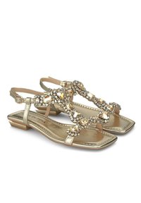 Sandalias planas doradas con diseño de tira en T, que presentan adornos de strass y un acabado metálico texturizado. Correa ajustable en el tobillo para un mejor ajuste.