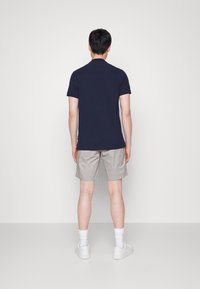 Polo shirt blu navy, pantaloni corti khaki, sneaker bianche e calzini alla caviglia; visualizzato da dietro su uno sfondo grigio uniforme.