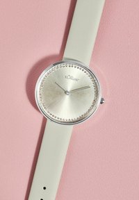 Runder silberner Uhr mit einem hellgrünen Lederarmband, ausgestattet mit einem strukturierten silbernen Zifferblatt und einem Ring aus Strasssteinen um die Lünette.