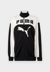 Mustvalge nööpidega jakk kõrge kaelusega, millel on esiküljel "PUMA" logo ja hüppav kassi graafika. Valmistatud siledast ja kergest kangast.