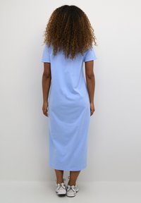 Svijetloplavi pamukasti haljinski t-shirt sa kratkim rukavima, opuštenog kroja i do koljena, uparen sa sivim tenisicama. Glatka tekstura, minimalni dizajn.