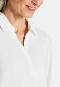 Witte blouse met een placketontwerp. Lichtgewicht, gladde stof benadrukt een schone, moderne uitstraling. Minimale stikseldetails zijn zichtbaar.