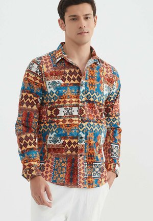 Chemise à manches longues présentant un motif géométrique et floral multicolore dans des tons de rouge, bleu et orange sur un fond clair, avec un col et des boutons.