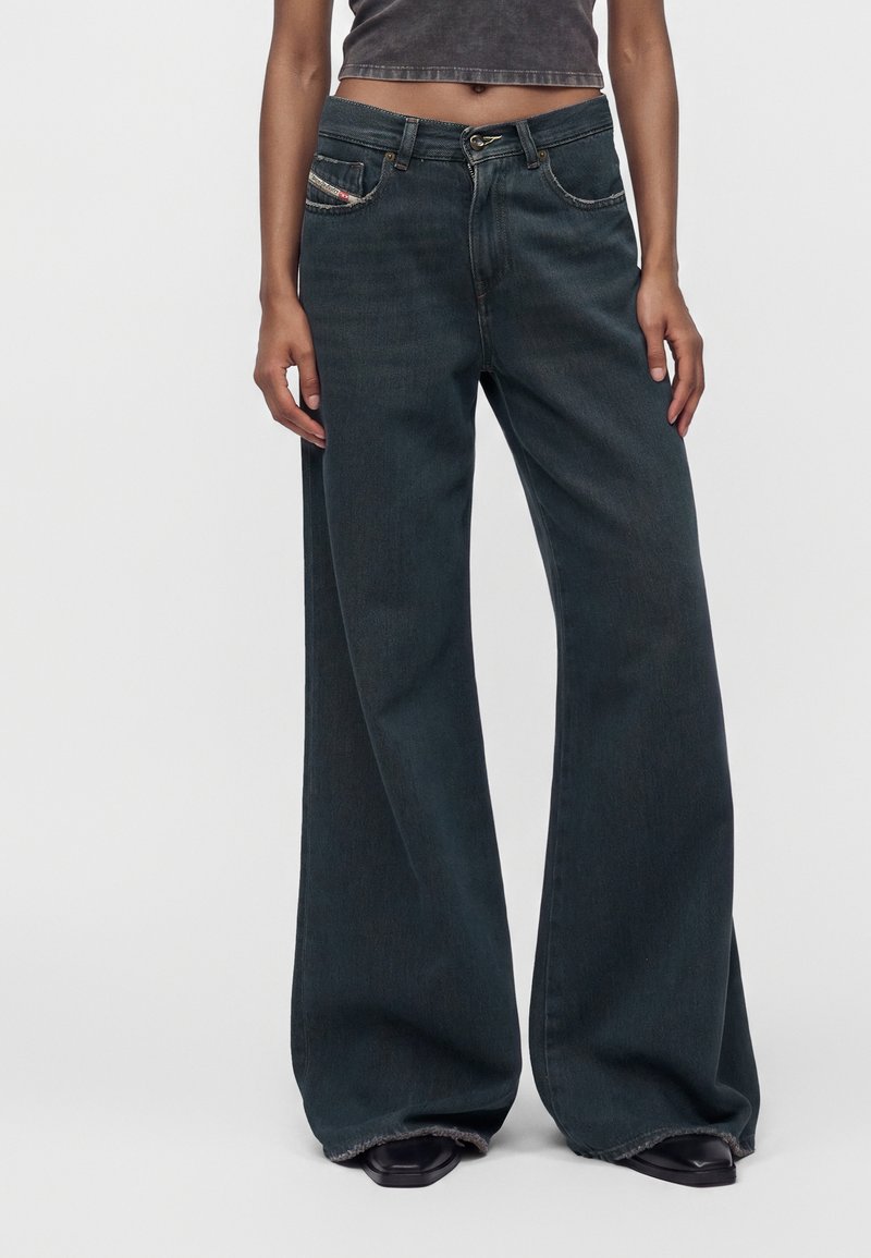 Personne portant un jean large foncé et un haut court gris foncé, debout avec les mains détendues le long du corps.
