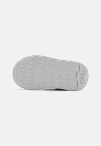 Hvitt gummisåle med teksturert mønster, med sirkulære og buede grep. "adidas"-logoen er preget på siden.
